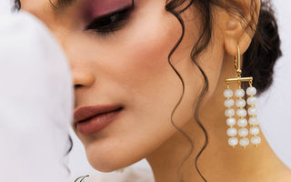 A close-up portrait of a young woman wearing minimal makeup and stylish gemstone jewelry, set against a soft, blurred background to highlight her natural elegance