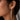 A close-up of a model's ear wearing a long, dangling 925 sterling silver, rhodium plated earring with multiple clear round gemstones.