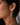 A close-up of a model's ear wearing a long, dangling 925 sterling silver, rhodium plated earring with multiple clear round gemstones.