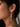 A close-up of a model's ear wearing a long, dangling 925 sterling silver, rhodium plated earring with multiple clear round gemstones.