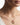 A close-up of a model wearing a delicate gold chain necklace with a small gold bow pendant featuring a vibrant pink gemstone at the center in 925 sterling silver 18k Gold
