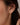 A close-up of a model's ear wearing a 925 sterling silver 18k gold plated dangle earring with clear round-cut gemstones.