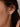 A close-up of a model's ear wearing a 925 sterling silver 18k gold plated dangle earring with clear round-cut gemstones.