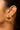 A close-up of a model's ear wearing  925 sterling silver 18K Gold-plated statement stud earrings featuring clear quartz gemstones in an intricate circular openwork design alongside a small silver stud earring.
