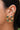 A close-up of a person's ear showing a 925 sterling silver earrings with five green oval stones, alongside other gold ear cuff with green stone
